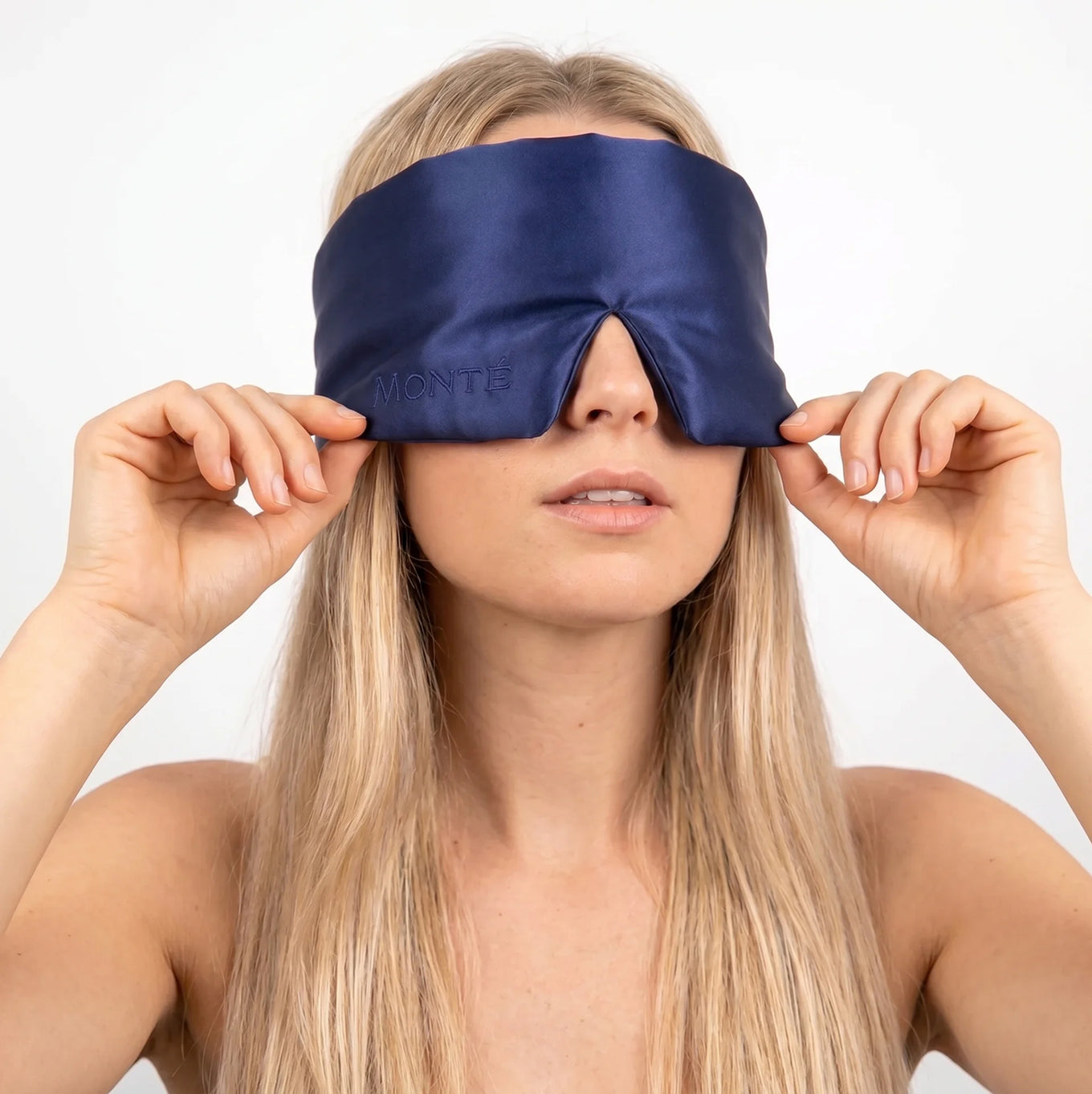 Monté midnight blue silk sleep mask held with both hands on a woman facing front – white background studio shot